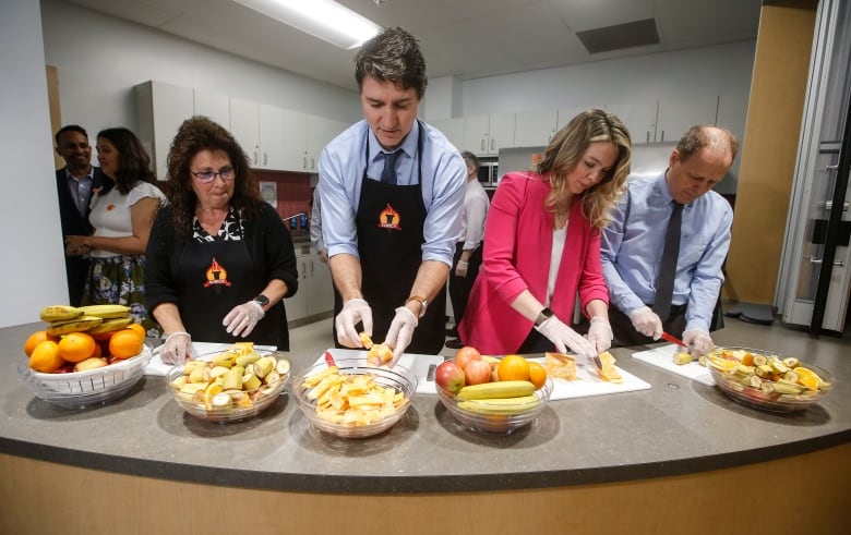 La asistente de educación Kim Jemielity (izquierda) corta fruta para los estudiantes que usan guantes desechables en el mostrador con el Primer Ministro Justin Trudeau, la Ministra de Desarrollo Social Jenna Sudds y el diputado liberal Kevin Lamoureux el 17 de mayo en la Escuela Comunitaria Elwick en Winnipeg. 