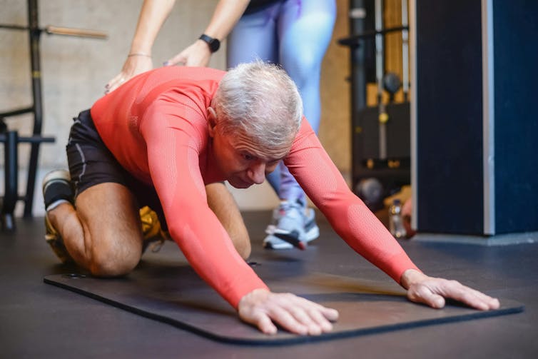 Un hombre se estira mientras un instructor de Pilates le da la espalda.