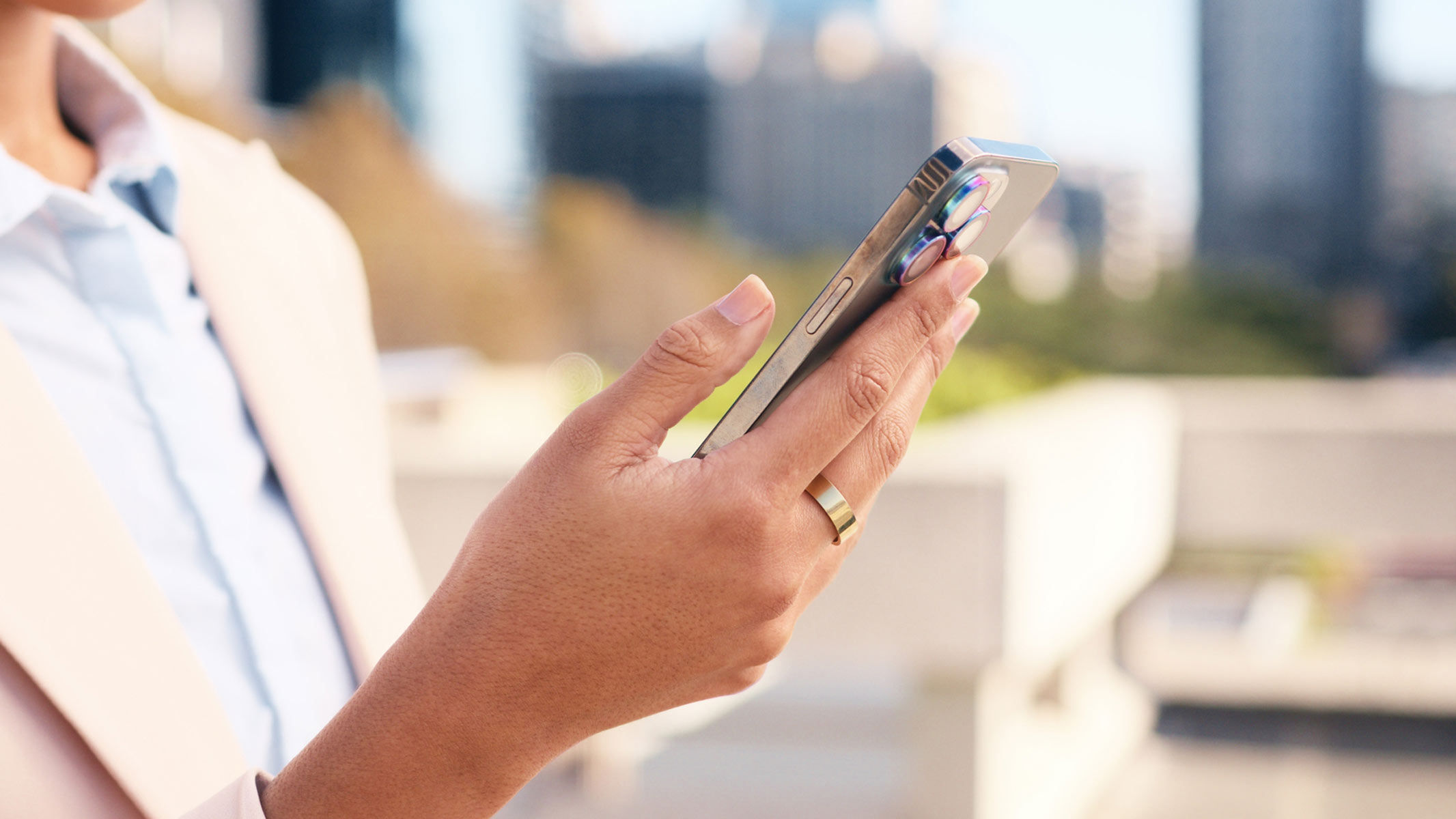 Una imagen cercana de la mano de una mujer sosteniendo un anillo inteligente y un teléfono celular