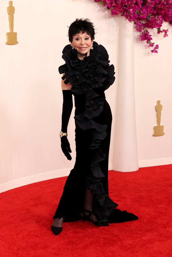 Rita Moreno destruyendo y sonriendo con un largo vestido negro con volantes
