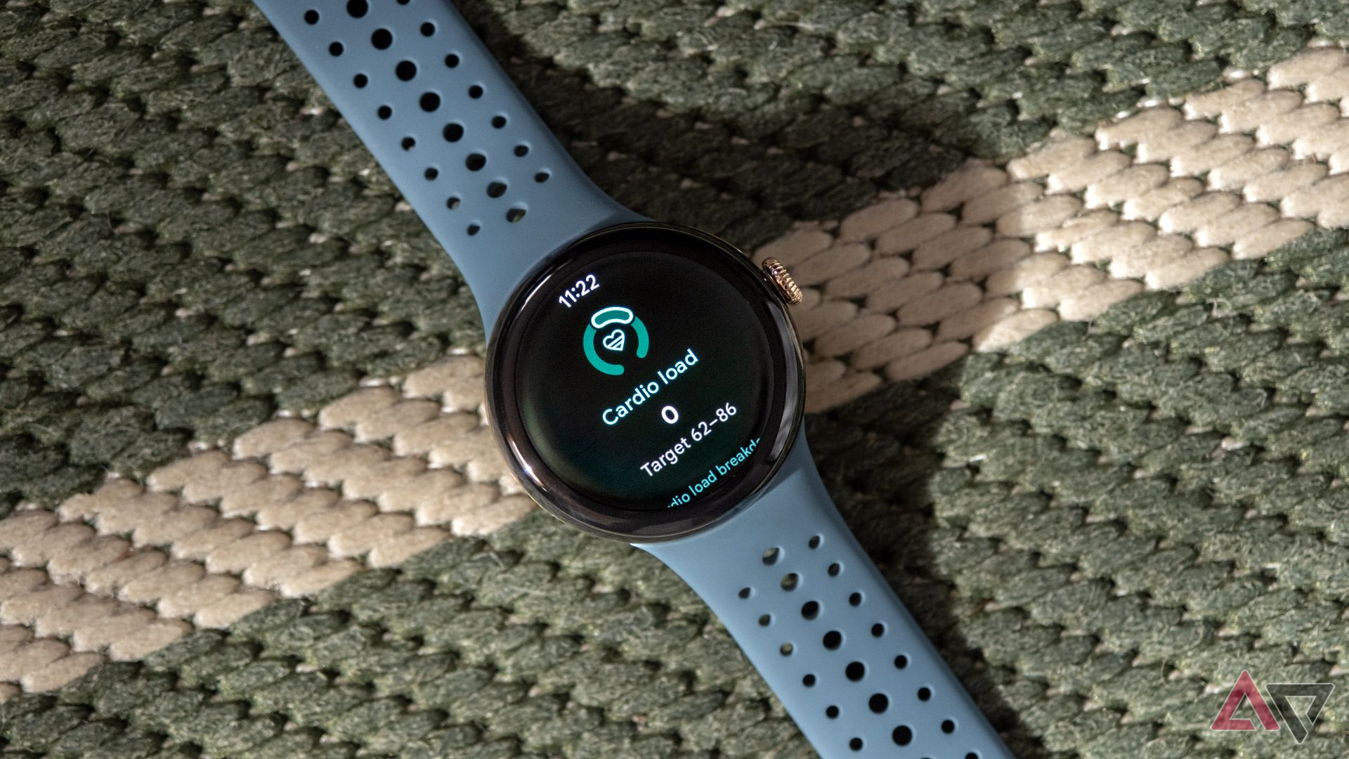 Google Pixel Watch 3 se encuentra en la superficie tejida verde y blanca con la función de carga cardiovascular en la pantalla. 