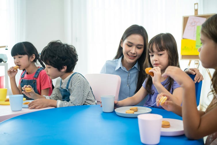 Niños que comen bocadillos con un maestro en la escuela