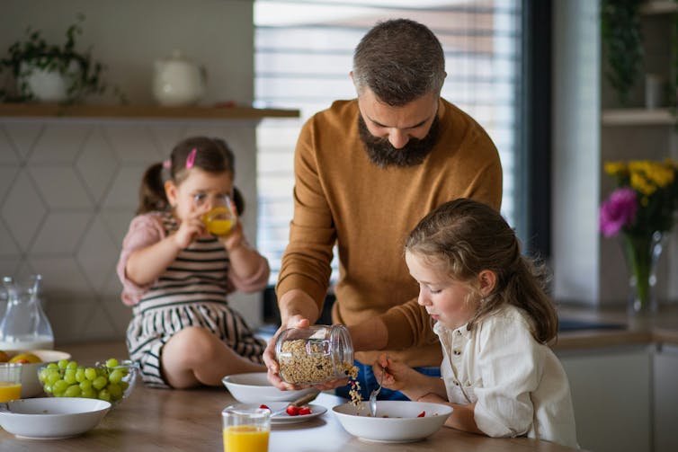 Un hombre en una cocina con dos niñas, arrojan un grano grueso para uno de ellos