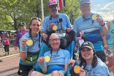 David, Alice y otros posan con medallas en la línea de meta del maratón de Londres.