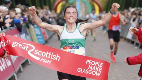 Gran Escocia, 'Katie' y 'Katie' y 'Castle Harriers', un corredor que estudia una serie de velas blancas y verdes, cruzaron la línea de meta de la gran carrera escocesa. La cinta de acabado se lee 