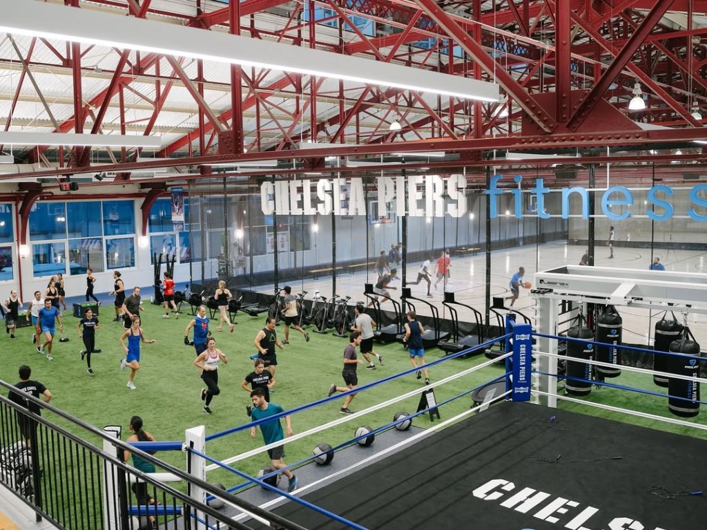 Una instalación deportiva cubierta con gente entrenando en un césped verde, un ring de boxeo y una cancha de baloncesto. 