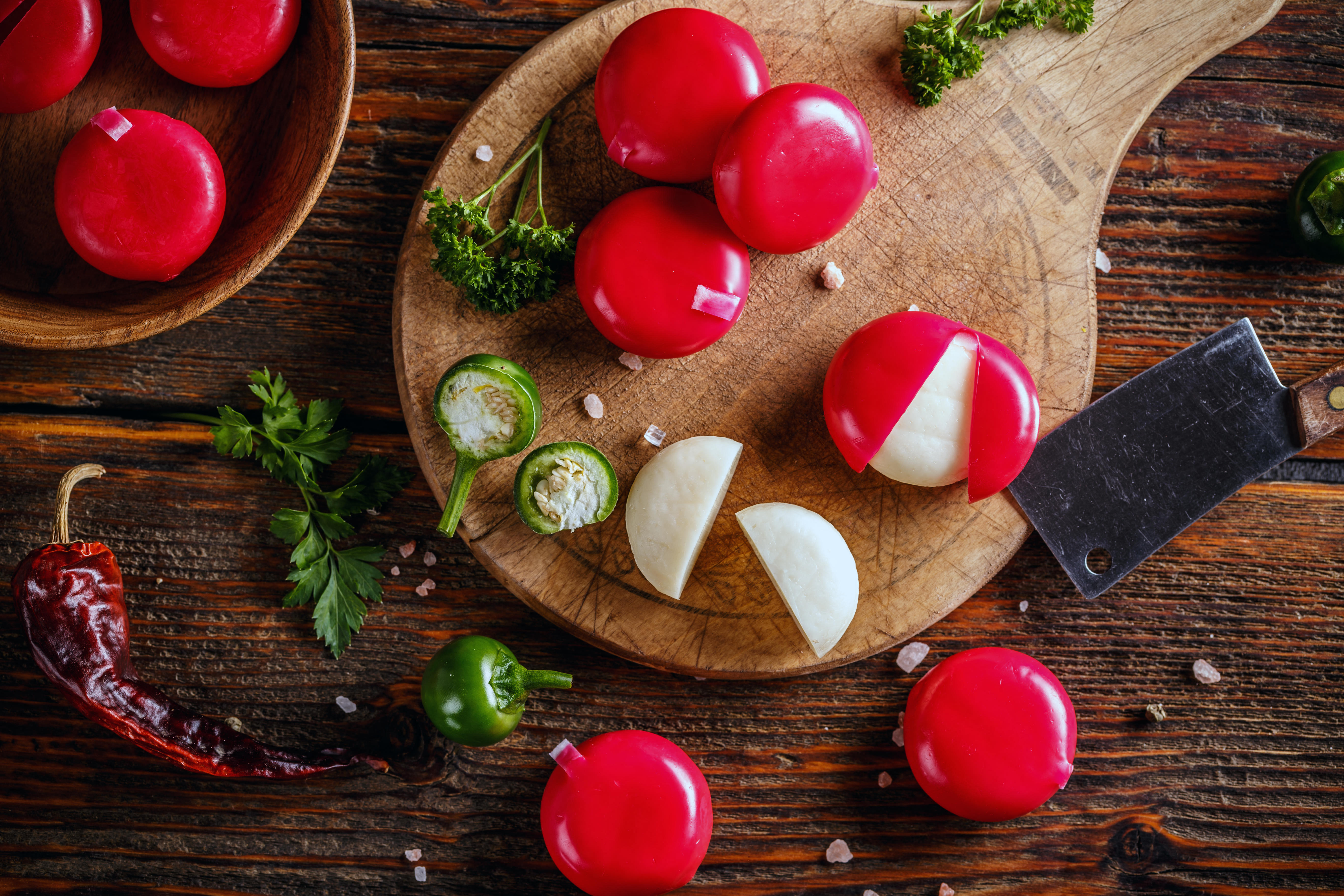 Vista superior del queso babybel elaborado con cera roja, algunos sin envolver sobre una mesa de madera con especias.