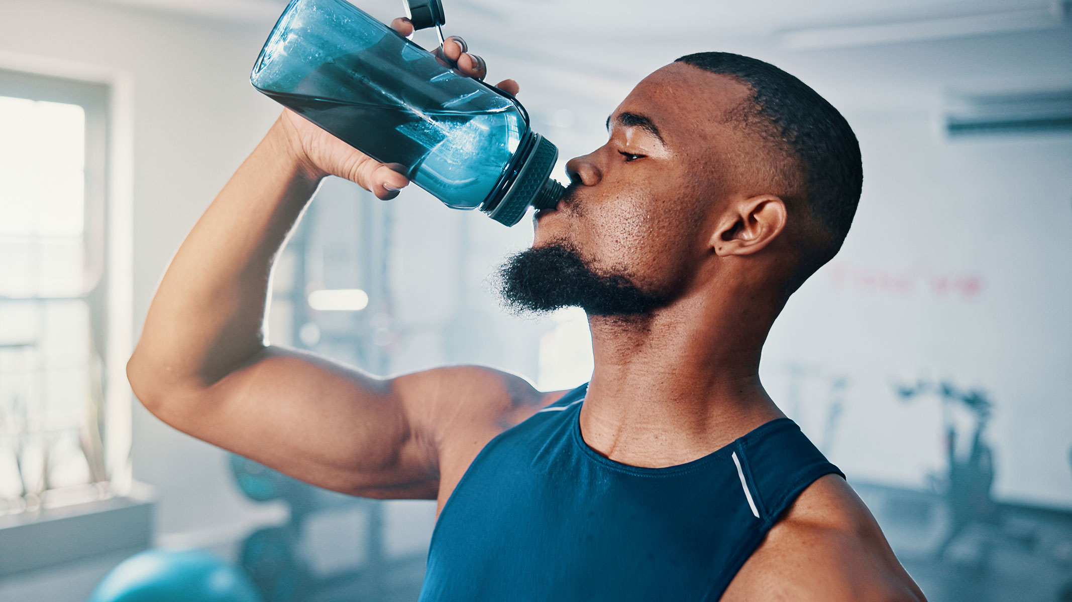 Un primer plano de un joven bebiendo agua de una botella en el gimnasio.