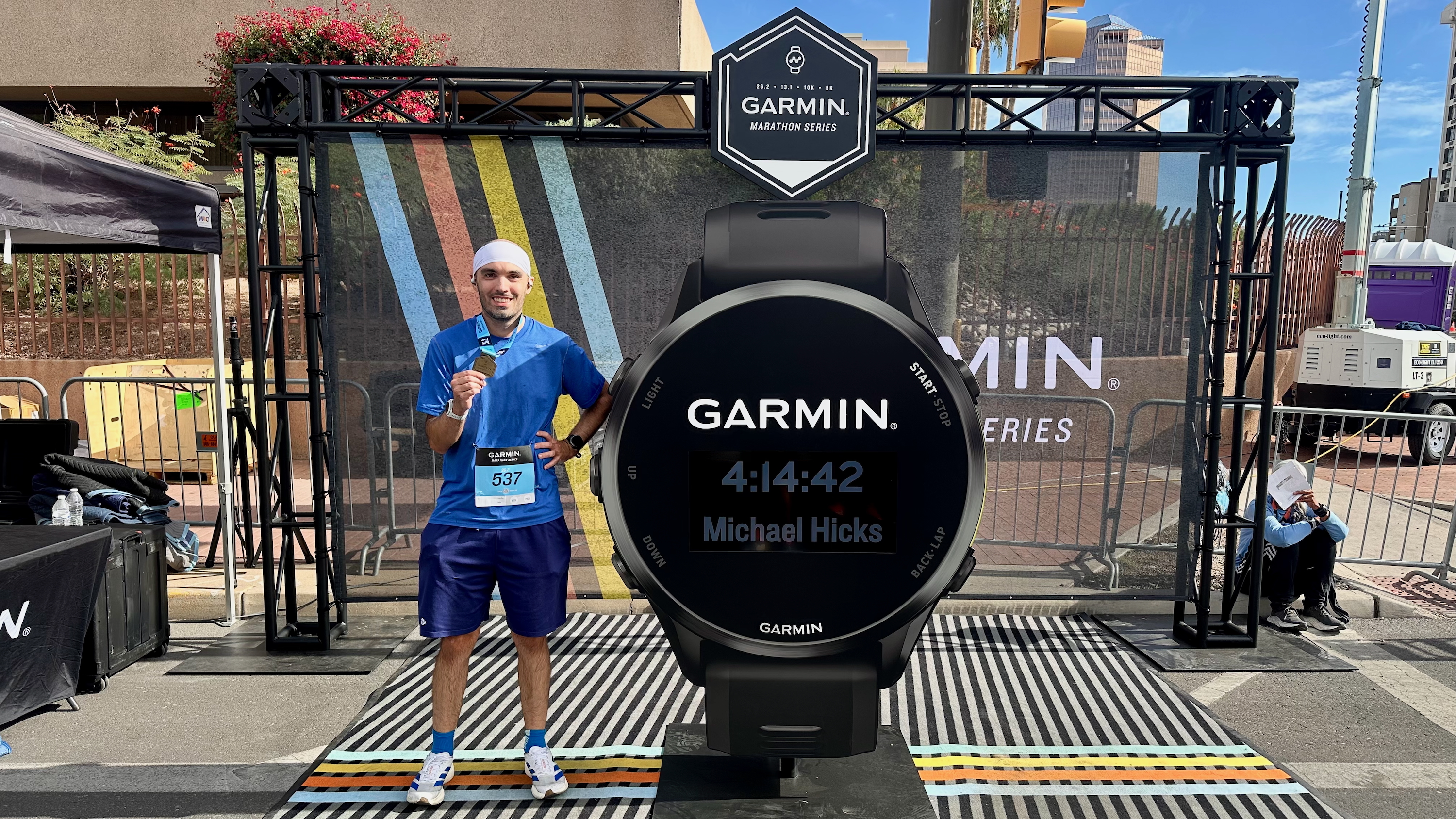 Una foto de Michael Hicks junto a un reloj Garmin gigante que muestra su tiempo en el maratón.