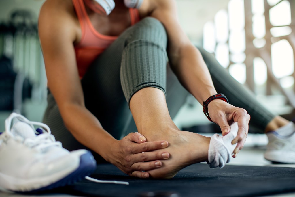 Mujer sosteniendo su tobillo lesionado con dolor después de hacer ejercicio en el gimnasio.