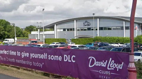 Vista de la calle del gimnasio David Lloyd con el cartel morado frente al aparcamiento en Google Derby