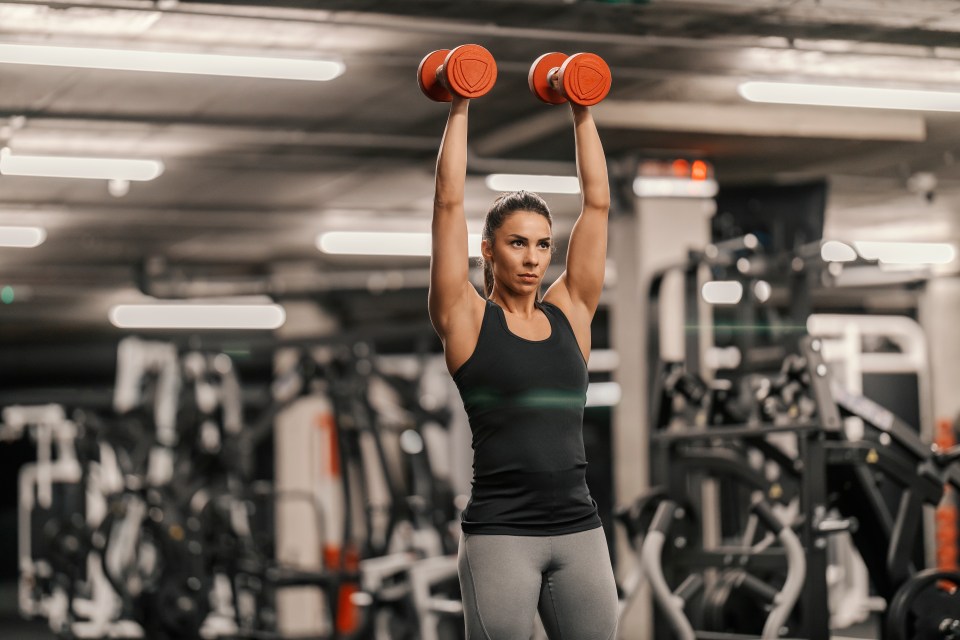 Mujer de mediana edad realizando prensas con mancuernas en el gimnasio.