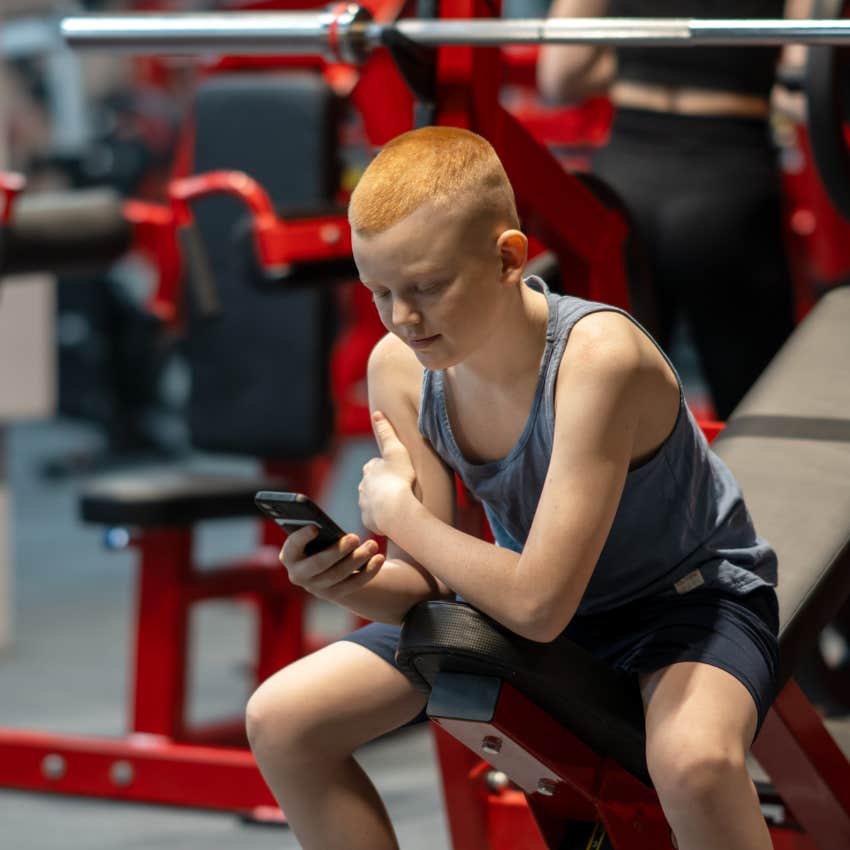 Joven viendo contenido de fitness por teléfono en el gimnasio sintiéndose inseguro